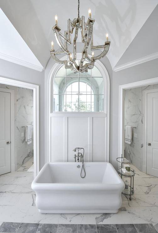 arch window walk in shower with large chandelier and tub in front
