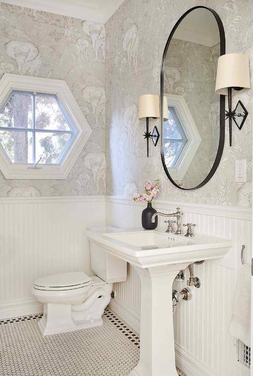 black frame oval mirror in half bath with pedestal sink wall sconces on either side toilet