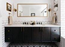 Bathroom features a full length gold mirror flanked by long brass and glass sconces and white subway tiles with black grout over a black dual bath vanity with marble look countertop and oil rubbed bronze vintage faucets and black mosaic floor tiles.