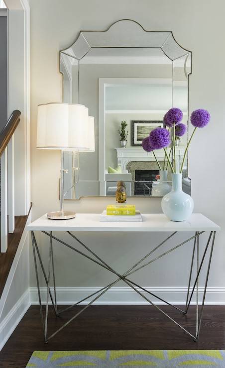 entryway vignette with console table topped with Table Lamp stacked with books and a modern white vase filled with aliums in front of an antiqued mirror framed mirror.