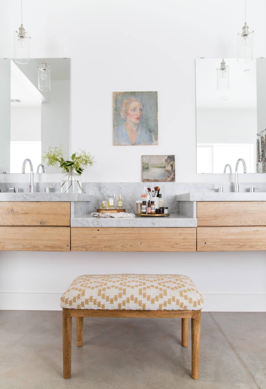 modern art in master bathroom with wood vanities stool to sit on white walls and marble countertops