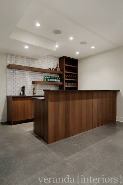 Fantastic wet bar/kitchen area in bright open basement! Gray tiled floors, wood paneled bar, granite counters and open shelving.