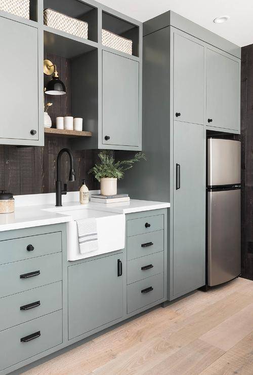 Cottage basement laundry room featuring green inset cabinets surrounding a fridge completed with a small farm sink and an oil rubbed bronze gooseneck faucet.