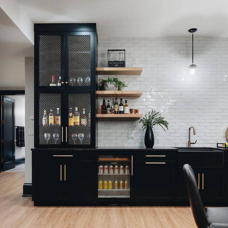 Basement wet bar with black lattice front cabinets features a glass front beverage fridge and oak floating shelves gray glazed offset tiles.