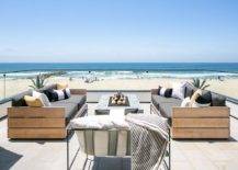 Beachfront outdoor patio features teak slatted outdoor sofas with a concrete fire pit on pavers finished with a glass enclosure.