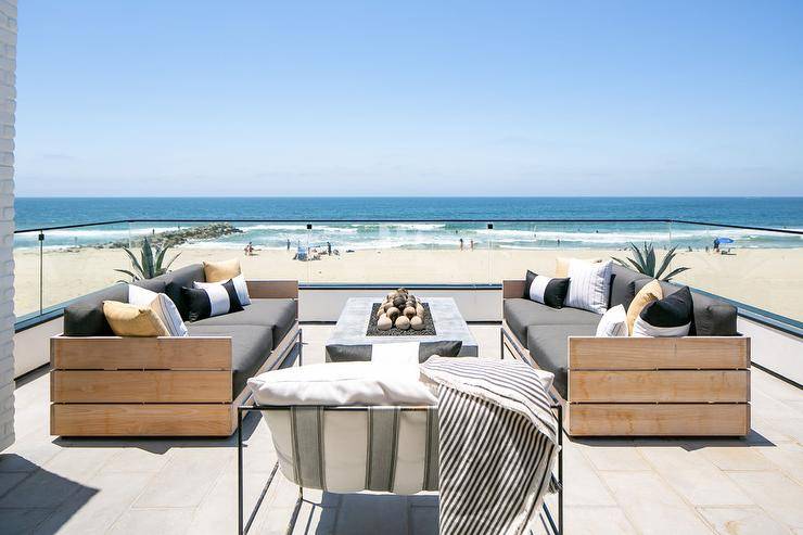 Beachfront outdoor patio features teak slatted outdoor sofas with a concrete fire pit on pavers finished with a glass enclosure.