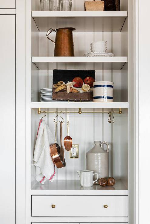 A small, beadboard trimmed nook is filled with shelves and brass hooks with copper pots and pans.
