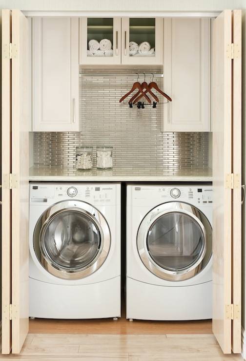 Chic small laundry nook with white washer & dryer, stainless steel linear tiles backsplash, white cabinets and folding doors.