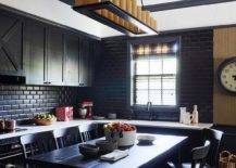 Black oak kitchen cabinets are mounted against black beveled backsplash tiles over a white countertop accenting black lower cabinets, while black oak stools sit at a black bar-height island. White upper walls are lined with black crown moldings.