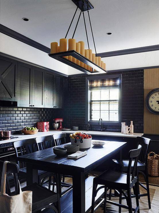 Black oak kitchen cabinets are mounted against black beveled backsplash tiles over a white countertop accenting black lower cabinets, while black oak stools sit at a black bar-height island. White upper walls are lined with black crown moldings.