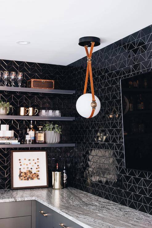 Contemporary wet bar features glossy black geometric tiles, black floating shelves and a flatscreen TV illuminated by a white glass and leather sphere pendant.