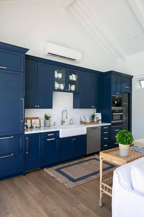 Blue kitchenette with a farm sink and stainless steel dishwasher in a cottage pool house features a split AC system above blue cabinetry.