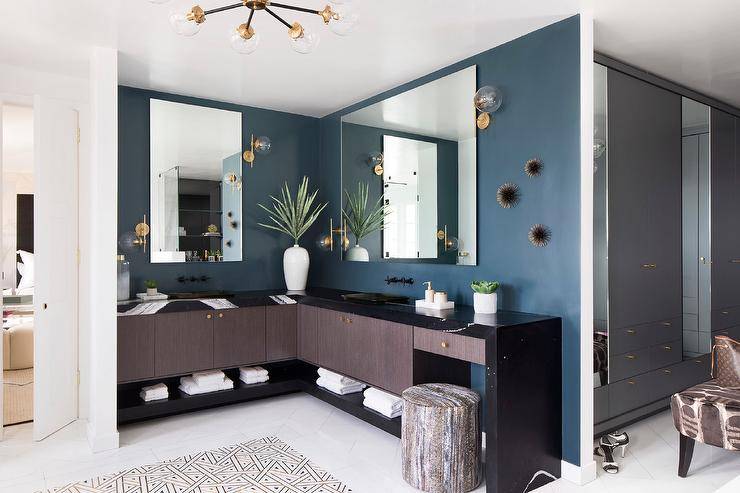Brown and blue master bath features a L shaped dual washstand in brown veneer accented with a black quartz waterfall edge on a blue wall.