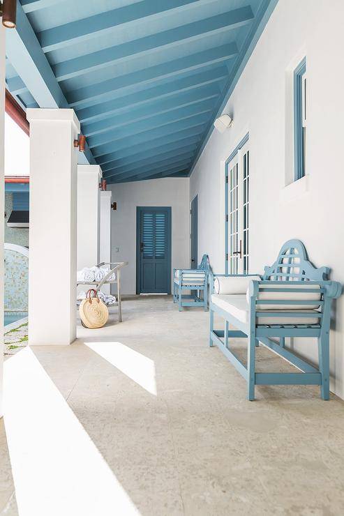 Cottage covered patio features a blue wooden bench under a blue plank ceiling matching window frames and doors.