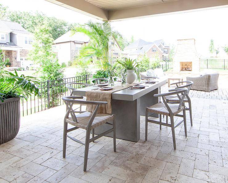 Hans Wegner Wishbone Chairs surround a concrete dining table fitted on a covered patio to cream pavers.