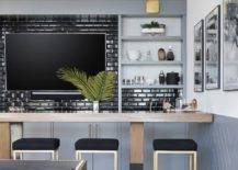 Contemporary wet bar features a TV mounted on black beveled subway tiles, a brown and black bar with gold and black barstools and built in shelves.