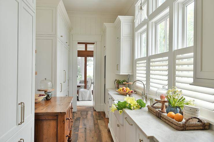 Cottage kitchen features a pantry with farmhouse island and white cabinets with a honed marble countertop.