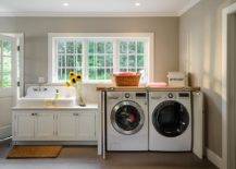 cottage laundry room features a vintage white porcelain sink next to a cabinet concealing a washer and dryer in cabinet with fold in doors placed under windows.