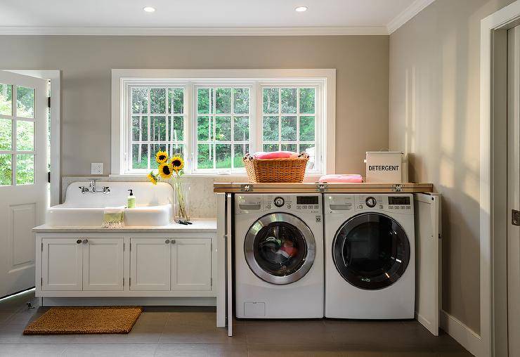 cottage laundry room features a vintage white porcelain sink next to a cabinet concealing a washer and dryer in cabinet with fold in doors placed under windows.