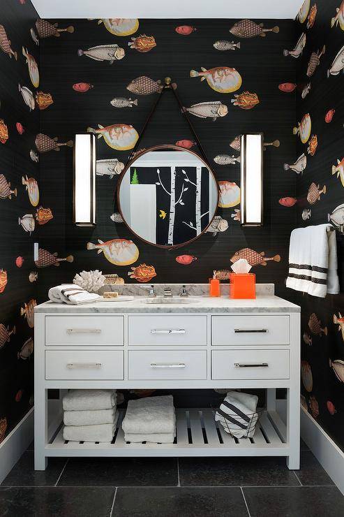 orange and black fish themed pattern wallpaper in a transitional bathroom with a Restoration Hardware Hutton Single Extra-Wide Washstand with a slatted shelf accented with polished nickel pulls. Carrera marble vanity top around the bathroom sink and nickel faucet are highlighted by a set of nickel and glass box sconces lighting up a unique and fun bathroom design.