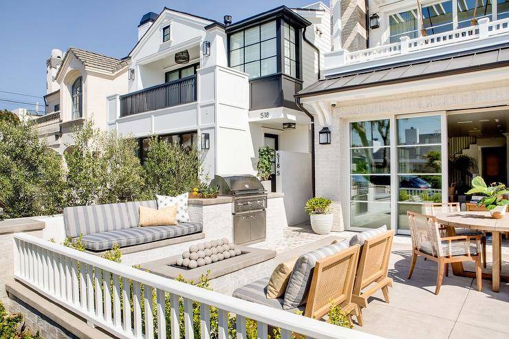 Beautifully appointed patio features a white brick fire pit placed between a white brick sofa topped with gray striped cushions and side-by-side teak lounge chairs.