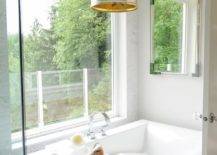 Master bathroom features a modern freestanding tub accented with a lucite tray and a deck mount gooseneck tub filler placed under a picture window illuminated by a bold pendant.