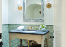 Chic powder room features a skylight illuminating a white and black bone inlay mirror flanked by scalloped brass wall sconces, Hudson Valley Lighting Pomona Sconces, as well as a beige washstand topped with honed black marble.