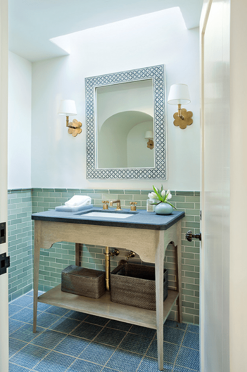 Chic powder room features a skylight illuminating a white and black bone inlay mirror flanked by scalloped brass wall sconces, Hudson Valley Lighting Pomona Sconces, as well as a beige washstand topped with honed black marble.