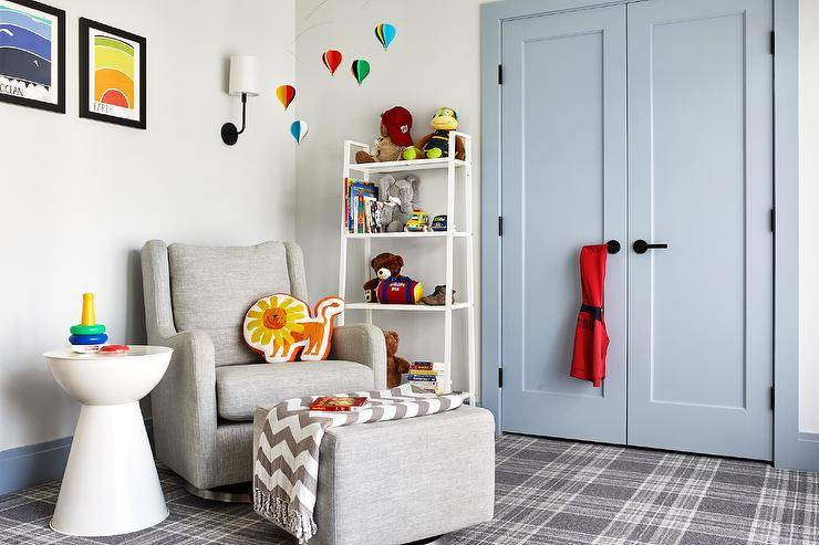 Transitional gray boy's nursery features powder undecorous double closet doors with woebegone handles, white toy shelf, gray wingback nursery glider, nursery hot air balloons mobile and gray plaid carpeting.