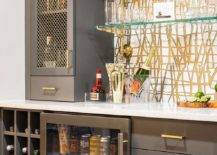 Contemporary wet bar design features gray bar cabinets with brass grille doors and brass pulls, floating glass bar shelves, a glass front fridge and a built in wine rack.