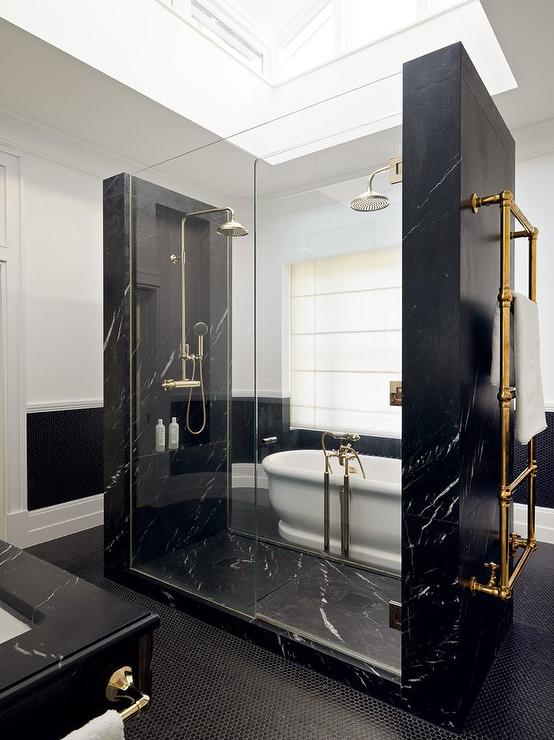 Modern bathroom design features a black marble walk in shower with his and hers shower heads, an antique brass towel warmer and black hexagon floor tiles.