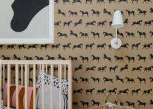 Contemporary boy's nursery features tan and black equestrian wallpaper, a blond wooden nursery crib and black and white art and a woven basket.