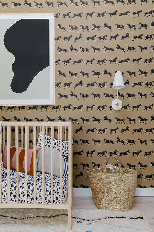 Contemporary boy's nursery features tan and black equestrian wallpaper, a blond wooden nursery crib and black and white art and a woven basket.