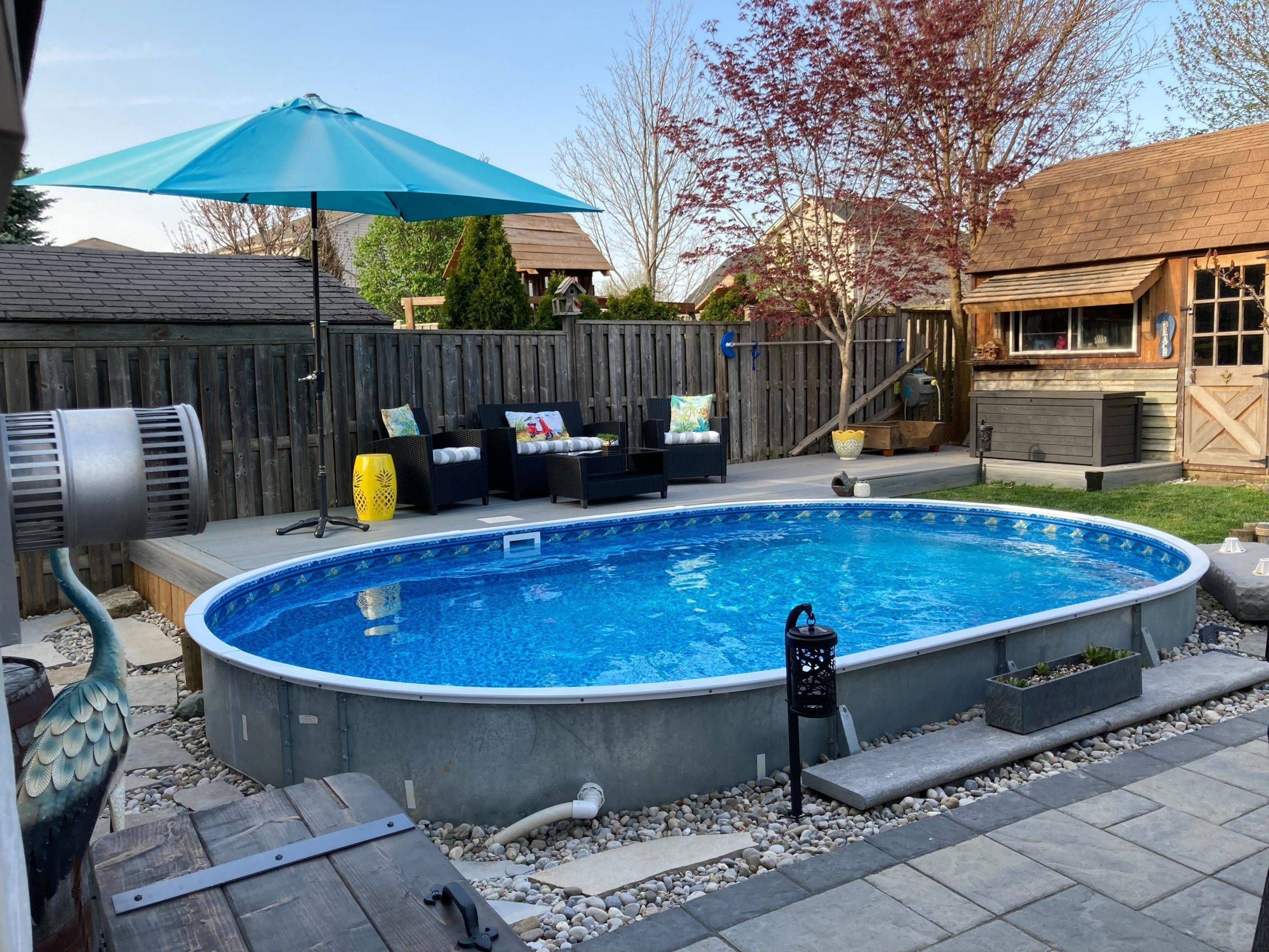 inground pool on grey stone patio with blue umbrella and lounge chairs