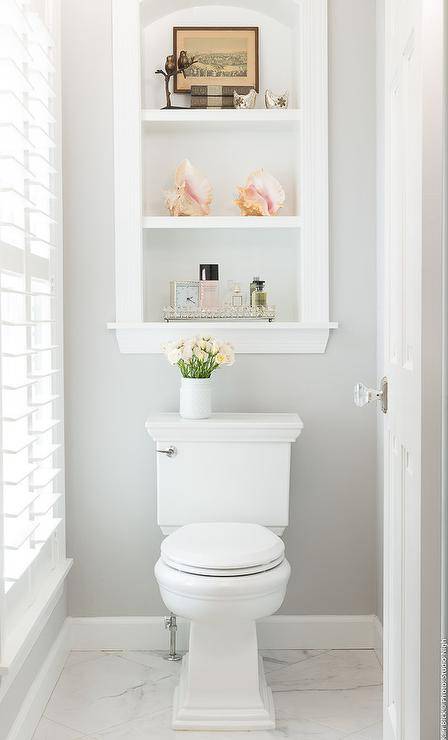 Custom inset shelves over a toilet in a transitional white and gray bathroom. Marble floors take on a classy template to the bathroom design with a polished appeal.