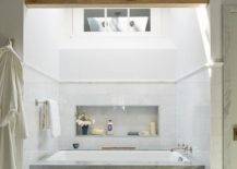A gorgeous trestle ceiling accents a bathroom boasting a skylight located over a marble clad drop-in bathtub fixed to white and gray marble mosaic floor tiles against a marble tiled wall. A large niche is located about the tub.