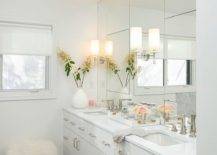 Glam white master bathroom featuring pops of pink for soft accents invites a chic appeal. Off white double washstand with a white quartz countertop and a paneled vanity mirror completed with a gray marble hexagon floor creates a well designed and timless space.
