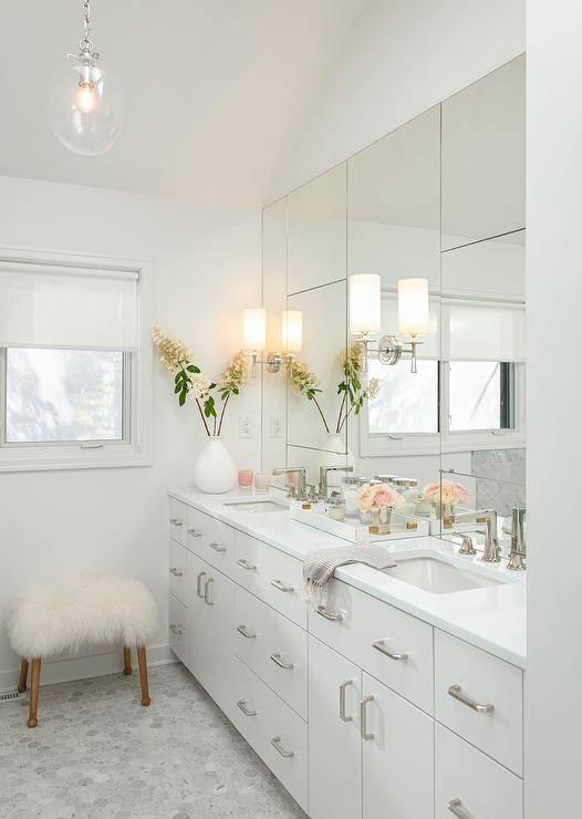 Glam white master bathroom featuring pops of pink for soft accents invites a chic appeal. Off white double washstand with a white quartz countertop and a paneled vanity mirror completed with a gray marble hexagon floor creates a well designed and timless space.