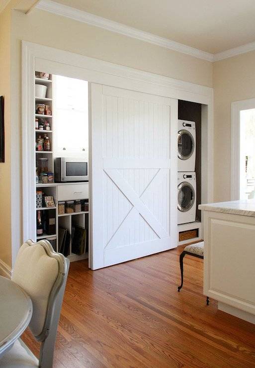 Walls painted in Valspar Cream in My Coffee frame white sliding barn doors which open up to reveal a hidden pantry and a stackable front loading washer.