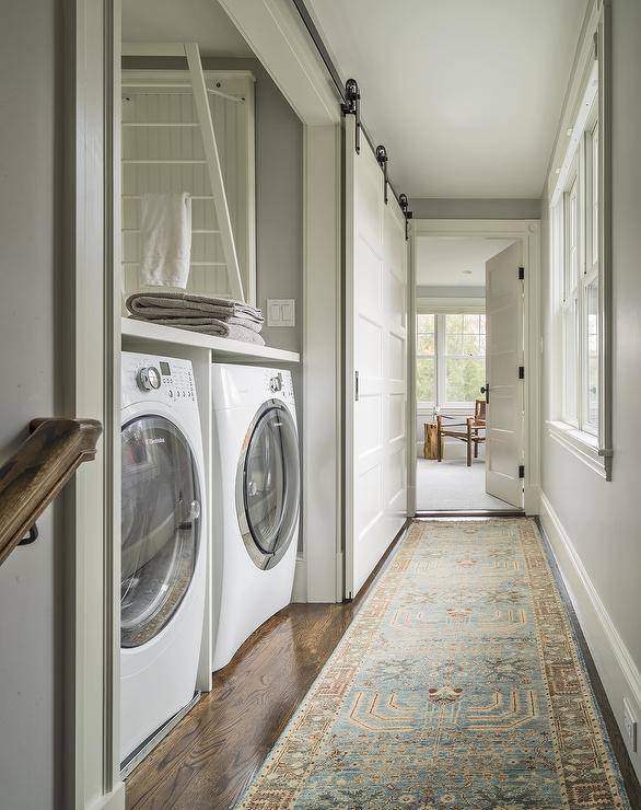 Chic hallway laundry room features a sliding barn door on rails opening to a washer and dryer tucked under a folding table as well as a wall mount drop down drying rack.