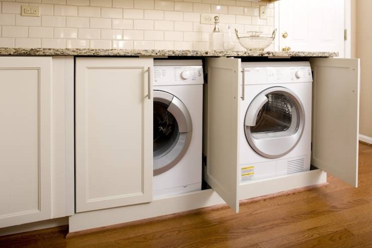 fabulous laundry room features white front-load washer and dryer hidden behind shaker cabinets paired with granite countertops and subway tile backsplash.
