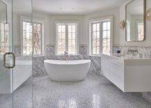 Master bathroom bay windows are partially framed by a gray marble slab backsplash and are positioned over an oval freestanding bathtub with a polsihed nickel floor mount tub filler fixed against marble hexagon floor tiles.