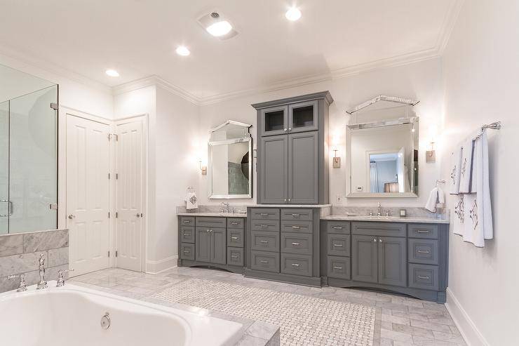 Stunning bathroom features separate gray washstands topped with carrera marble under Global Views Governor's Palace Mirrors flanking gray storage cabinets. Grey master bathroom boasts a marble clad tub next to a seamless glass shower.