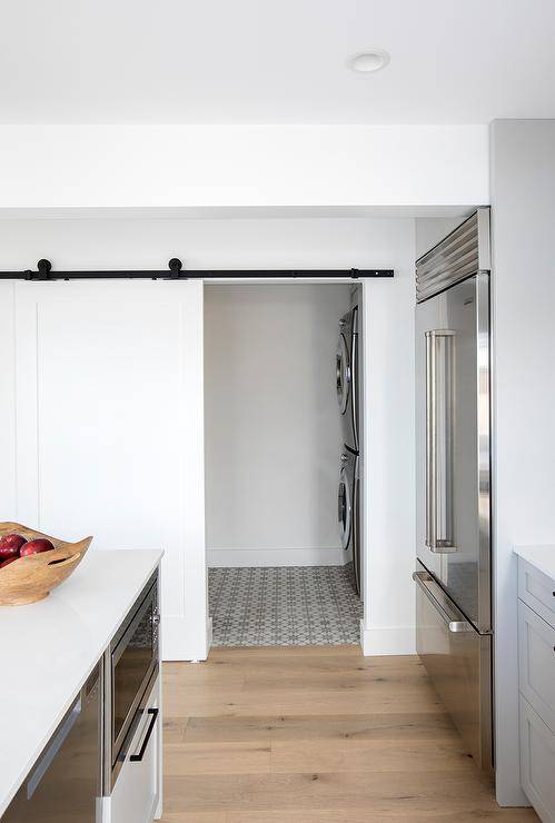 Laundry room designed with a white sliding door on an oil rubbed bronze rail showcasing gray cement tiles and stacked front load washer and dryer.