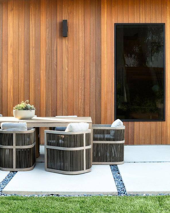 Restoration Hardware Capri Teak Armchairs sit at a gray outdoor dining table placed on concrete pavers framed by black river rocks.