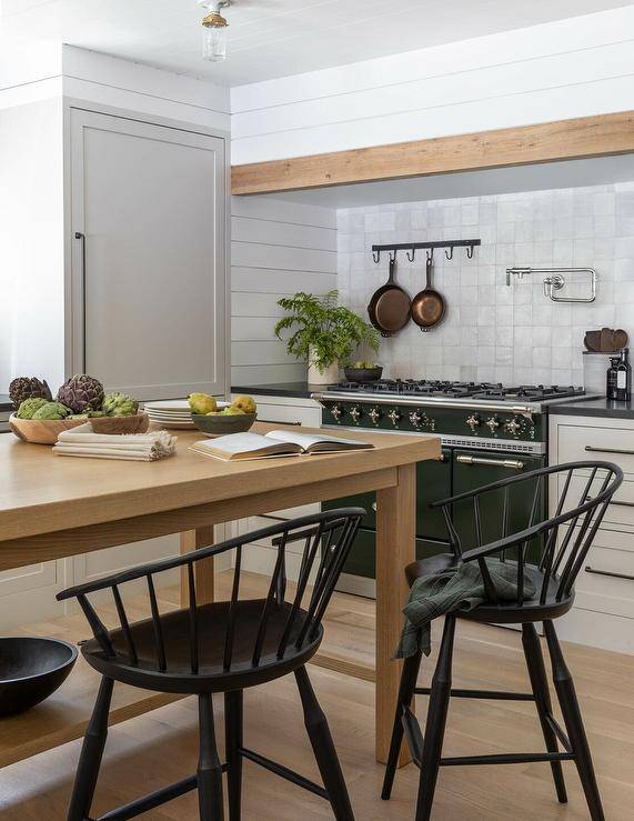 Cottage kitchen features black spindle stools at a brown wooden freestanding island.