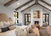 Vertical shiplap fireplace wall in a master bedroom furnished with elegant gray and wood-carved chairs uniting with a woven coffee table decorated with stacked books.