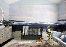 Contemporary blue and gray boy's nursery features black nursery crib, a gray French dresser, a light gray sofa rocker with green avocado accent table, a brown cowhide rug and a blue and gray wall mural.