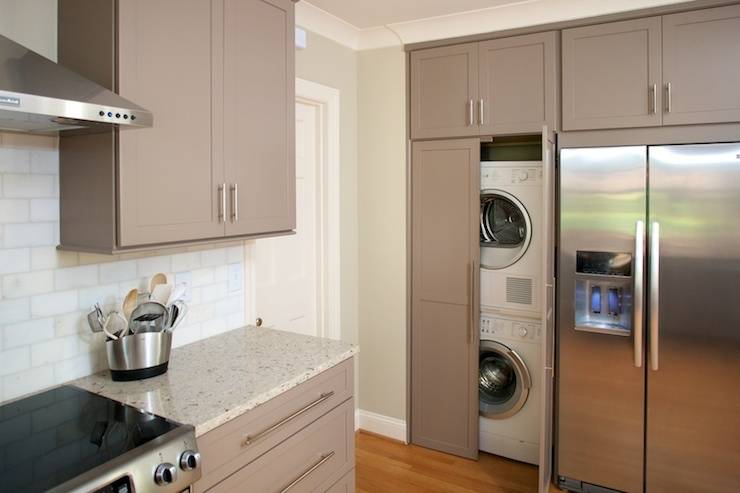 Kitchen features taupe cabinets paired with granite countertops and subway tile backsplash. Kitchen with stacked washer and dryer hidden behind cabinet doors next to French door refrigerator.