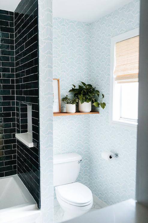 Wood floating shelf over a toilet adds a charming touch mounted on a white and blue wallpaper wall displaying plants and a wooden frame.